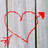 Red heart-shaped line drawing with arrow tip on right end, set against light gray background with vertical dark stripes.