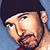 Pixelated static icon of a person's face with dark hair and beard, light skin tone, blue background, visible facial features including eyes, nose, mouth, and ear, rendered in low-resolution style with dithering effects.