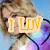 A pixelated image of a person with blonde hair wearing a purple and white outfit against a light blue background, featuring overlaid text in different colors.