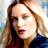 Pixelated static image of a person with long light brown hair wearing dark clothing and red lipstick, set against a blurred background with blue and green tones.