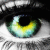 A close-up of a human eye with green and yellow irises, black pupil, visible eyelashes, and light skin tones surrounding the eye.