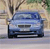 A blue sedan car icon with a blurred background of trees and sky, viewed from the front.