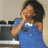 Pixelated image of a person in blue clothing with hands near face, set against light background and dark furniture.
