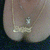 A gold necklace with a nameplate pendant and small charm rests on a person's chest, visible through a low-cut top.