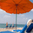 A pixelated beach scene with an orange umbrella, blue water, and a person in a blue swimsuit on the right.