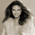 Static grayscale image of a person with long dark hair wearing light-colored clothing against a neutral background.