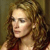 Pixelated close-up of a person with light brown curly hair, wearing a dark red garment, against a muted brown background.
