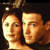 Pixelated static image of two human faces in close-up, side-by-side with dark background and warm lighting.