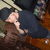 A person in dark clothing lies on a wooden floor with a bottle nearby, viewed from above in a static image.
