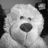 A grayscale pixelated image of a dog's face with a rounded snout and dark eyes, set against a dark background with lighter side elements.