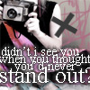 A person holding a silver camera with a black lens, wearing a black sleeveless top with a large black X on the shoulder, pink and orange straps, and a pink and purple patterned garment, with overlaid white text reading "didn't see you when you thought you'd never stand out?".