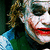 Pixelated close-up of a character with white face paint, dark eye makeup, and red lips smiling widely against a green background.