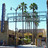 Pixelated static image of a building with tall smokestacks, palm trees, and a light blue sky background.