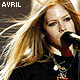 A four- shows a person with long blonde hair singing into a microphone, wearing dark clothing and layered necklaces against a brown background
