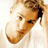 Pixelated close-up of a person's face with light brown hair tied back, visible eyes and nose, and partial white clothing against a plain background.