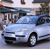 A light blue sedan with dark trim appears in a pixelated image, positioned on a road with blurred background elements suggesting motion.