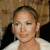 A pixelated close-up of a person with light skin tone wearing a white top and dark outer garment, set against a blurred brown background.