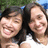 Two people with dark hair smiling closely together against a blurred green and blue background.