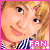 Pixelated close-up of a smiling person with light brown hair, wearing a checkered shirt and pink border.
