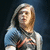 Pixelated image of a person with light brown hair wearing a blue and white shirt against dark background.