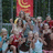 Pixelated group photo with pink text overlays on black background, showing multiple people in outdoor setting with red banner.
