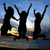 Silhouettes of three people jumping with arms raised against a blue sky and distant mountains.