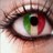 A close-up of a human eye with green and red vertical color bands across the iris, dark eyelashes, and light skin tones surrounding the eye.