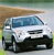 Pixelated image of a white van with blue-tinted windows and black wheels, positioned on a light gray surface against a blurred background of green and brown tones.