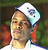 Pixelated static image of a person wearing a white head covering with blue and light blue accents, set against a blurred background with green and red tones.