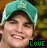 A person wearing a teal cap with white trim and dark brim, smiling broadly against a blurred green-brown background.