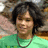 Pixelated static image of a person with dark curly hair wearing a green top and silver necklace against blurred background.