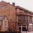 Pixelated static image of a building with brown and beige tones, featuring a prominent roofline and partial architectural details.