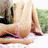 A person lies on a white surface with green foliage in the background, transitioning from a seated pose to a reclined pose with legs extended.