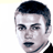 Static pixelated icon of a person's face with short dark hair, visible facial features including eyes and mouth, wearing a white collared shirt under a dark jacket or suit against a plain background.