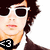 Pixelated image of a person with dark curly hair, white sunglasses, and a black choker necklace, wearing a white shirt and dark jacket.