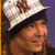 Pixelated close-up of a person wearing a white and black cap with brown accents, smiling against a purple background.