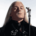 nine shows a person with long light hair in a black jacket with white patterns, standing before a microphone, with green text reading "Lucius Malfoy" overlaid on each