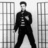Black-and-white image of a person in dark clothing standing between two -patterned structures on an orange background with pixelated text