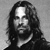 Black-and-white pixelated portrait of a person with long hair, beard, and mustache, wearing a dark shirt against a gradient background.