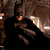 Batman in dark cowl and cape, standing against a textured background with light reflections.