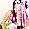 A static image of a person with long pink and purple hair wearing a colorful bikini top and multiple necklaces, holding a white object.