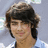 Pixelated static image of a person with dark hair and light skin, wearing a blue garment against a blurred background.