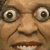 Pixelated close-up of a face with large round eyes, brown eyebrows, and visible teeth in a neutral expression.