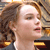 Pixelated close-up of a person with light brown hair, closed eyes, and a neutral expression, wearing a dark top with light straps.