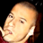 Static pixelated image of a person's face with light skin tone, visible eyes and nose, and partial red clothing against black background.
