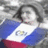 A person holds a flag with blue, white, and red stripes and a central emblem, positioned against a blurred background.