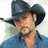 Pixelated image of a person wearing a dark cowboy hat and blue shirt, holding an object near their face.