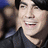 A person with dark hair and a black shirt smiles broadly across three showing slight head movement