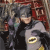 Batman character in gray suit with yellow bat symbol on chest, black cape and mask, performing sequential hand movements against red background