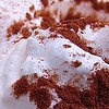 A close-up of a dessert with white frosting and brown crumbly toppings on a light surface.